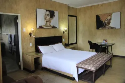 a bedroom with a large white bed and a table at South Gate Lodge in Polokwane