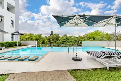 a swimming pool with lounge chairs and an umbrella at Nosivu@Regency Apartment Hotel in Pretoria
