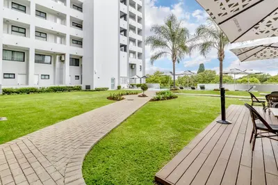 a patio with tables and chairs and a grass yard at Nosivu@Regency Apartment Hotel in Pretoria