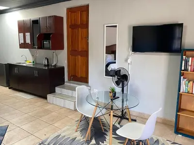 a living room with a glass table and a kitchen at Waterkloof Glen Guest House in Pretoria