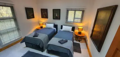 a bedroom with two beds and a table and windows at Luxury GuesthouseCo RiverHouse in Marloth Park
