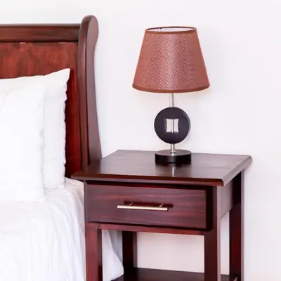 a nightstand with a lamp on it next to a bed at In The Bush Farm Lodge in Winterveld