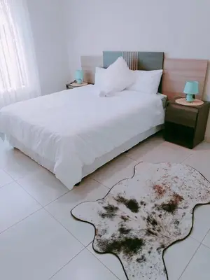 a bedroom with a white bed and a rug on the floor at Reutlwane Gardens Apartments in Secunda