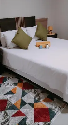 a bedroom with a white bed with a colorful rug at Reutlwane Gardens Apartments in Secunda