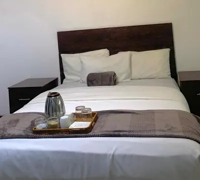 a bed with a tray of food and two glasses on it at Khaya Mnandi Leisure Suites in Pretoria
