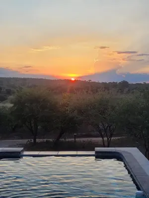 a swimming pool with a sunset in the background at Rosendal Kruger View Villa in Marloth Park