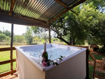 a hot tub with a bottle and glasses in it at Crooked Cottage in Pelindaba