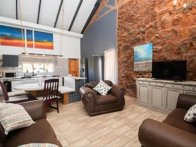 a living room with a couch and chairs and a kitchen at Crooked Cottage in Pelindaba