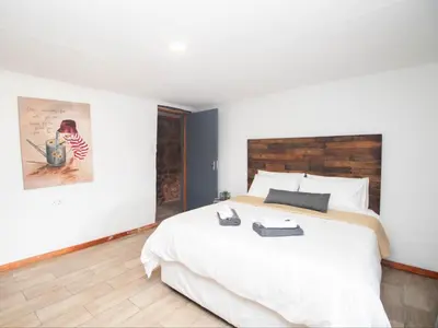 a bedroom with a large white bed with a wooden headboard at Crooked Cottage in Pelindaba