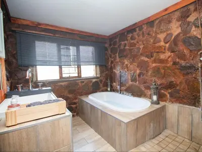 a bathroom with a large tub and a stone wall at Crooked Cottage in Pelindaba