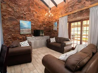 a living room with leather furniture and a stone wall at Crooked Cottage in Pelindaba