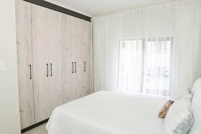 a white bedroom with a white bed and a window at The Ellipse Palazzo Apartment in Midrand
