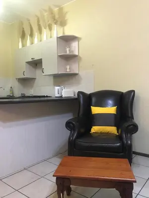 a black chair with a yellow pillow and a coffee table at White Rose Cozy Apartment in Midrand