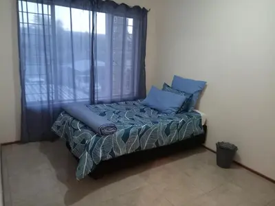 a bed with blue pillows in a room with a window at Alternate Cosy Home in Pretoria