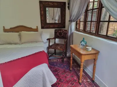a bedroom with a bed and a table and a chair at Cottage by the Woods in Pretoria