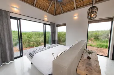 a bedroom with a large bed and large windows at Villa Zazu in Hoedspruit