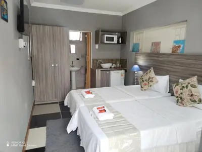 a bedroom with a large white bed and a kitchen at FUMODS guest house in Pretoria