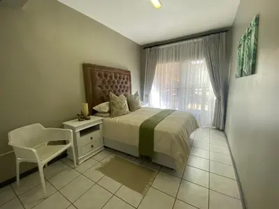 a bedroom with a bed and a chair and a window at AfricaLove on Tiger Suite in Pretoria