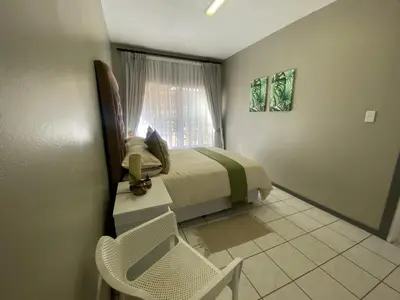a bedroom with a bed and a chair and a window at AfricaLove on Tiger Suite in Pretoria