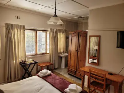 a bedroom with a bed and a desk and a mirror at Pebble Fountain Guesthouse in Pretoria
