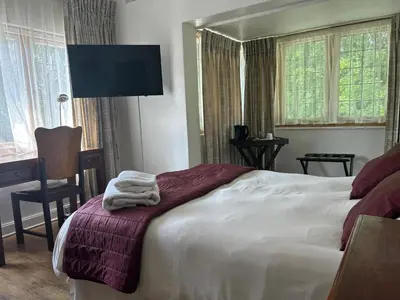 a bedroom with a bed and a desk and windows at Pebble Fountain Guesthouse in Pretoria