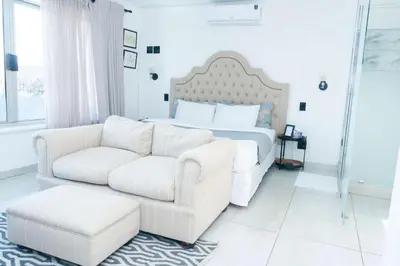 a white bedroom with a bed and a white couch at 129inHarties Lodge and SPA in Hartbeespoort