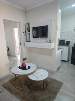 a living room with two tables and a tv on a wall at Peshline Guest House Unit 1 in Ermelo