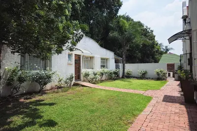 a white house with a grass yard and a driveway at Dutch on Tecoma, Wonderboom, Pretoria in Pretoria