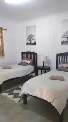 a bedroom with two beds and a table with a lamp at Paperbark Self Catering Units in Doornfontein