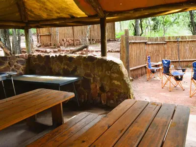 a patio with wooden tables and chairs and a stone wall at Masungulo Lodge in Modimolle
