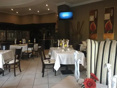 a restaurant with white tables and chairs and a tv at Witwater Guest House & Spa in Kempton Park
