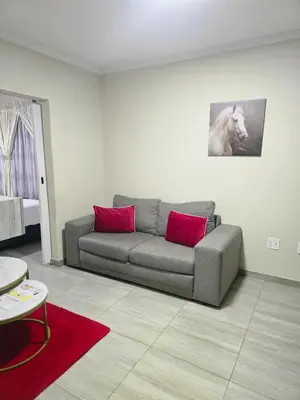 a living room with a couch with two red pillows at Peshline Guest House Unit 3 in Ermelo