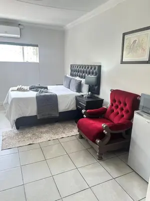 a bedroom with a bed and a red chair at Creekside Guest House Middelburg in Middelburg