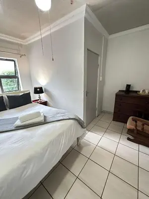 a white bedroom with a bed and a dresser at Creekside Guest House Middelburg in Middelburg