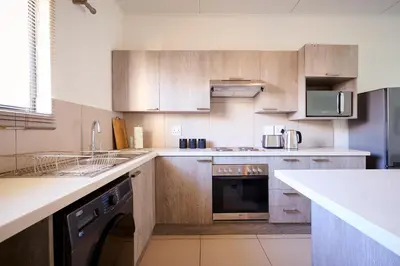 a kitchen with wooden cabinets and a dishwasher at Cozy Escape: 2 BR Apt. Sleeps 4 in Midrand