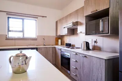 a kitchen with wooden cabinets and a tea kettle on a counter at Cozy Escape: 2 BR Apt. Sleeps 4 in Midrand