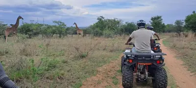 two people riding a dirt bike down a dirt road with giraffes at Casa de la Presa 2 in Polokwane
