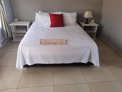a bedroom with a white bed with a red pillow at Monavy Riverside Hotels in Tzaneen in Lenyenye