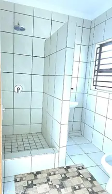 a white tiled bathroom with a shower and a sink at Monavy Riverside Hotels in Tzaneen in Lenyenye