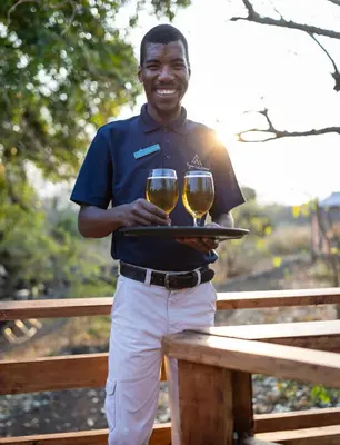 a man holding two glasses of wine on a tray at Kruger Untamed - Satara Plains Camp in Die Brug