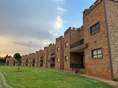 a row of brick buildings with a grass field at Castle Walk Estate in Roodeplaat