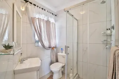 a white bathroom with a toilet and a shower at Cascade Villa Guesthouse in Secunda