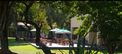 a patio with tables and umbrellas in a park at Nikita Portuguese Restaurant and Motel in Lanseria