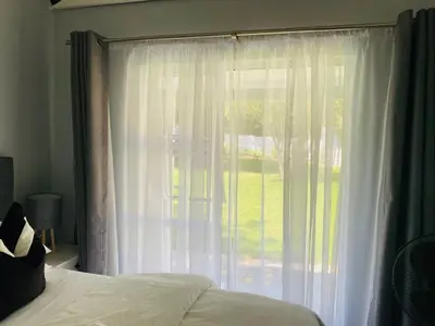a bedroom with a large window with white curtains at Cozy Guest Suite 2-with back up power in Midrand