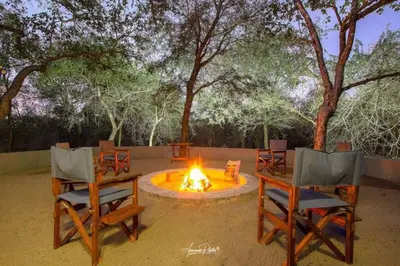 a fire pit with two chairs and a table and afire at Luxury GuesthouseCo Butterfly House in Marloth Park