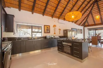 a large kitchen with black cabinets and a table at Luxury GuesthouseCo Butterfly House in Marloth Park