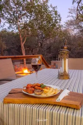 a plate of food and a glass of wine on a table at Luxury GuesthouseCo Butterfly House in Marloth Park