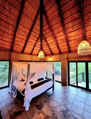 a bedroom with a bed in a room with windows at Luxury GuesthouseCo RiverDance in Marloth Park