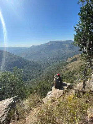 two people sitting on a rock overlooking a valley at Faith Cabin in Waterval-Onder