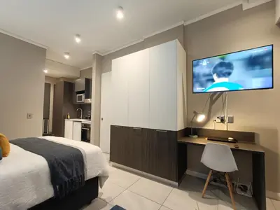 a bedroom with a bed and a desk with a tv on the wall at Comfort at 1320 Menlyn Maine Residences in Pretoria